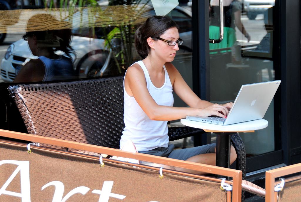 A woman works on her laptop from the comfort of a sidewalk cafe.