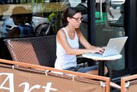 A woman works on her laptop from the comfort of a sidewalk cafe.