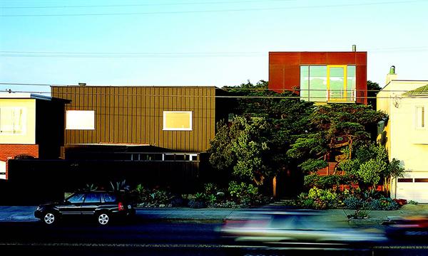 The addition (right side of image) nestles into the lush landscaping around the existing house (left side).