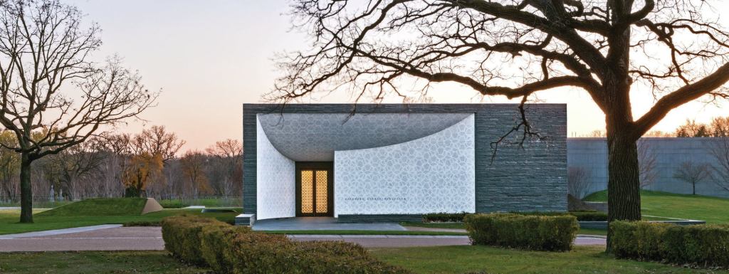 A view of the Lakewood Garden Mausoleum entry. The exterior materials include split-face gray granite. White mosaic tile surrounds the bronze entry doors.