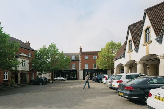 The first phase of Poundbury's construction included this village square, which is dominated by a market hall that was designed by John Simpson and that features an open undercroft and milk-bottle-shaped columns. Across the square sits The Poet Laureate, a pub.