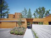 The landscaped entrance to the wood-clad Low/Rise House is at the end of a Vermont slate walkway, and flanked by a board-formed concrete wall that separates parking from private garden; the wall’s formwork was re-used as floor joists.