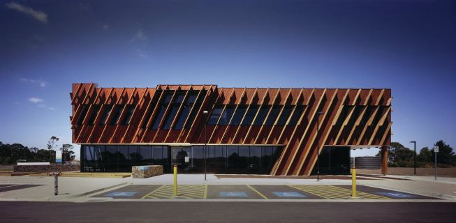 Pre-drilled boards attached with countersunk stainless steel screws hang at a 25-degree angle from the vertical axis clad the center’s roughly 6,000 square feet of façade.