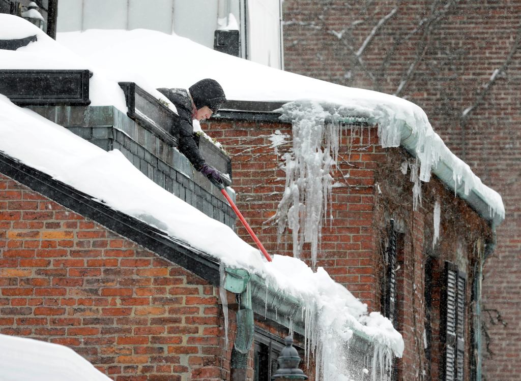 Susan Hartnett shovels snow from the roof of her Beacon Hill home in Boston.
