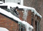 Susan Hartnett shovels snow from the roof of her Beacon Hill home in Boston.