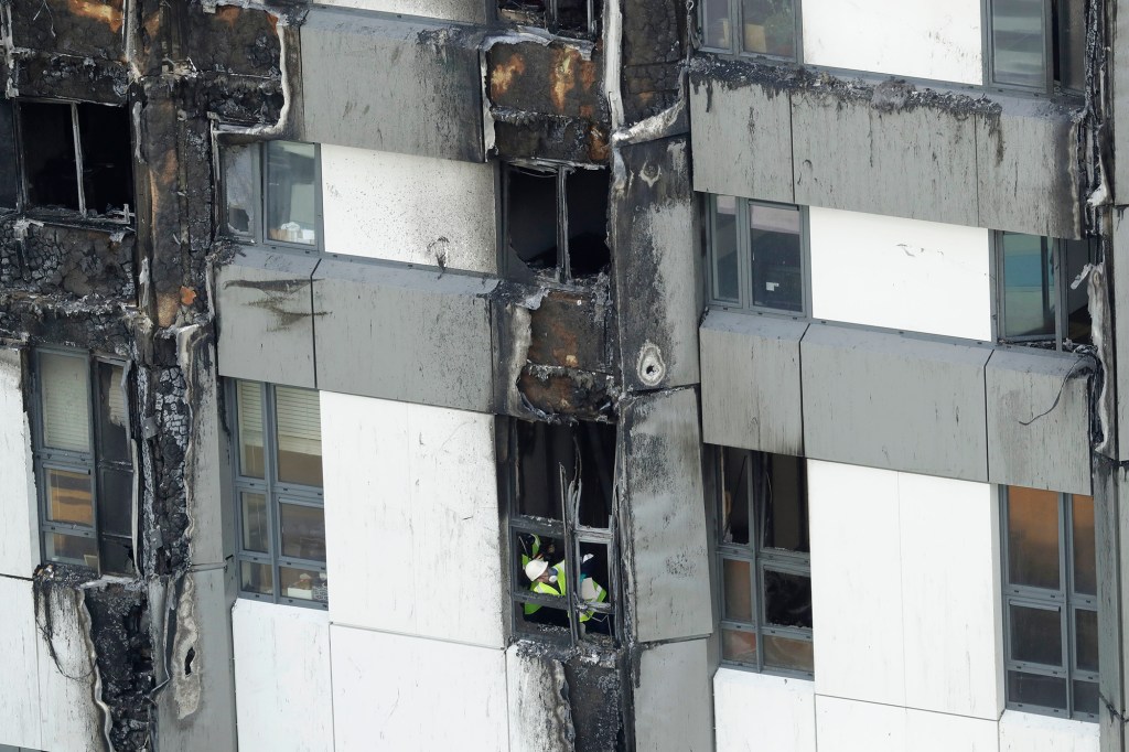 An emergency worker looks out from one of the lower floor windows of the fire-gutted Grenfell Tower in London, Friday, June 16, 2017, after a fire engulfed the 24-storey building on Wednesday morning. Grief over a high-rise tower blaze that killed dozens of people turned to outrage Friday amid suggestions that materials used in a recent renovation project may have contributed to the disaster.