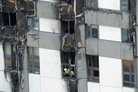 An emergency worker looks out from one of the lower floor windows of the fire-gutted Grenfell Tower in London, Friday, June 16, 2017, after a fire engulfed the 24-storey building on Wednesday morning. Grief over a high-rise tower blaze that killed dozens of people turned to outrage Friday amid suggestions that materials used in a recent renovation project may have contributed to the disaster.