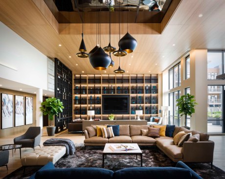 The second floor club room features natural elements, cool blue tones, and warm wood accents for a refined natural feel. A built-in bookshelf serves as the room’s focal point and anchors the tall space.