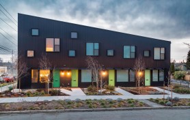 Corrugated metal, grooved plywood, and extra wide window flashings lend texture and depth to the monochromatic building. Front doors in shades of green add a pop of color.