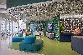 This dynamic lounge area and coffee bar brings together a unique curved ceiling, green accent wall, black and white tiled backsplash, and modern sofas to provide a flexible space that inspires community