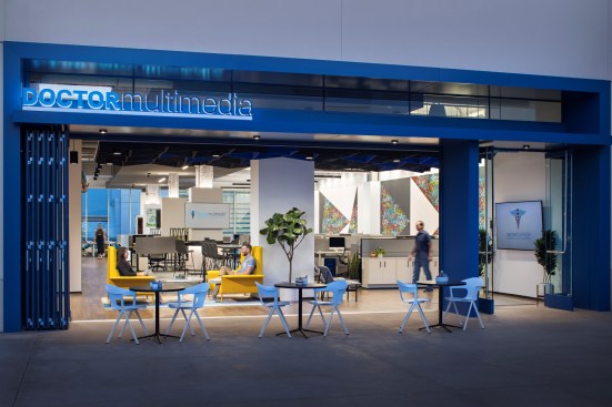 The inviting ground floor entrance features a public-facing glass door and large sliding windows, while the café tables and lounge chairs encourage community seating