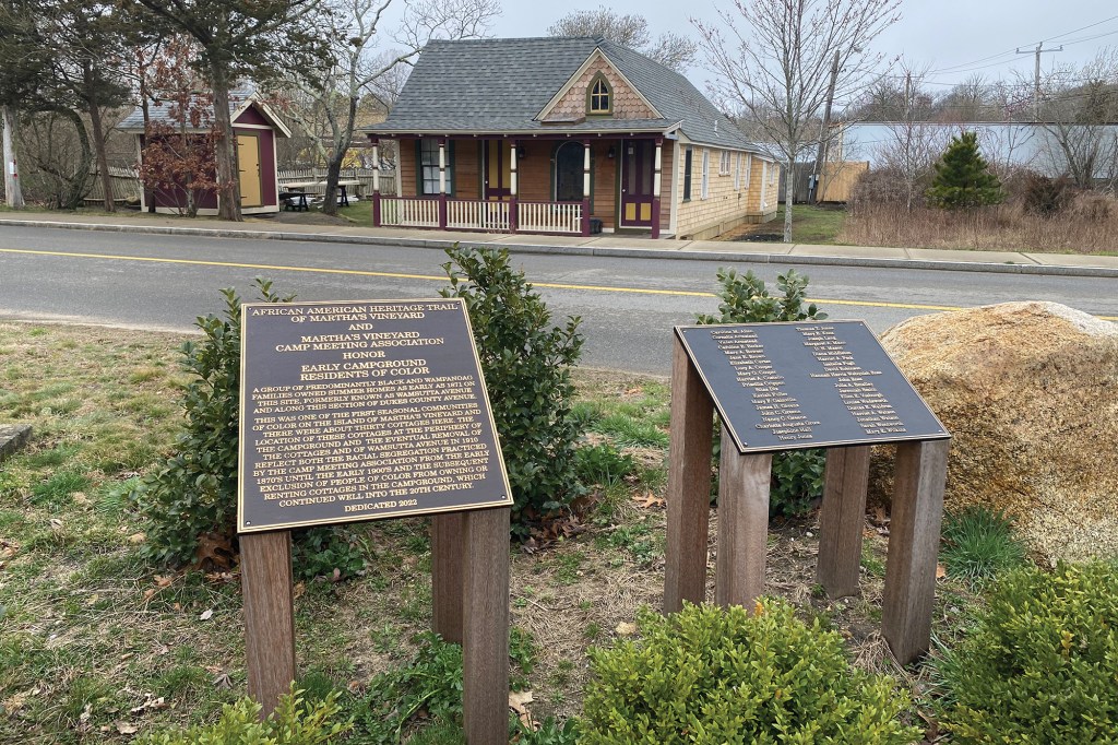 A plaque of the African American Heritage Trail of Martha’s Vineyard, with text co-authored by Fallon Samuels Aidoo. A cottage owned and occupied by African Americans in the late 19th century stands in the background on swampland.