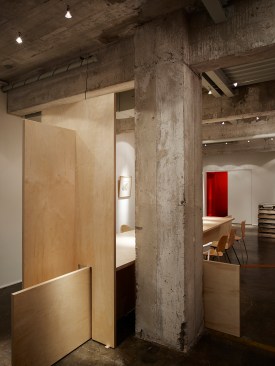 A+view+looking+east+past+a+historic+concrete+column.+The+slab+table+shows+respect+for+the+historic+building+by+passing+by+instead+of+engagement.++The+wood+pallet+hors+d%e2%80%99oeuvre+table+is+located+near+the+entrance.++A+cable+system+allows+artwork+to+be+relocated+without+wall+damage.++The+red+lighted+floor+trench+is+historic+and+originally+redirected+a+chronic+basement+leak+to+a+floor+drain.++We+installed+a+red+LED+light+in+the+trench+and+covered+it+with+perforated+weathering+brass+for+safety.++