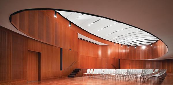 The double-height event oval is tucked into a lower level of the Diana Center. Available for everything from group yoga classes to alumnae events, it was an integral part of the program from the very beginning. Acoustical material is hidden behind bent wood panels and revealed by milled slats that mimic the pattern of the graduated frit on the curtain wall. For events that fill the space beyond capacity, the rest of the building is equipped with closed-circuit televisions.