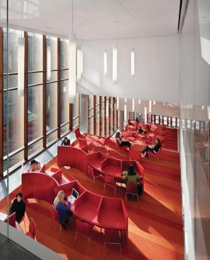 In the third-floor reading room, custom-designed, serpentine rows of carrels, as well as nooks tucked into the west wall, allow for private study. The architects custom-designed the carpet with Bentley Prince Street, and it transitions from deep red tones on the first floor toward oranges and yellows in each ascending atrium. The reading room overlooks the more formal dining area, which doubles as a study lounge in off-hours: "Once the dining service closes, that room stays full," says Gamsu. "Even though it's a double-height space, the proportions feel just right. The visual stimulus is just wonderful, but it's quiet and peaceful."