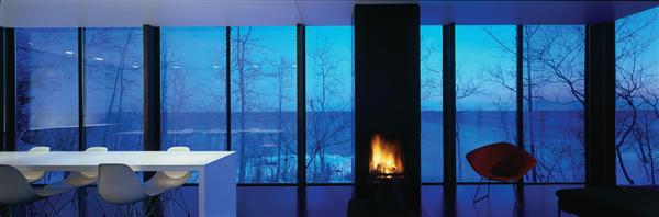 A white dining table runs through the main house, parallel to Lake Superior. The homes quiet design directs attention to the lake year-round, at all times of day.