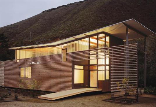 Fougerons thin butterfly roof and cedar rainscreen create a blithe facade. The one-story cedar-clad volume contains the houses utility areas and screens the glassy living spaces from the dirt road.