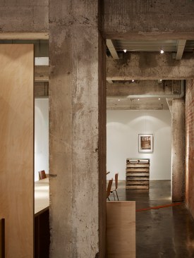 A+view+looking+east+past+a+historic+concrete+column.+The+slab+table+shows+respect+for+the+historic+building+by+passing+by+instead+of+engagement.++The+wood+pallet+hors+d%e2%80%99oeuvre+table+is+located+near+the+entrance.++A+cable+system+allows+artwork+to+be+relocated+without+wall+damage.++The+red+lighted+floor+trench+is+historic+and+originally+redirected+a+chronic+basement+leak+to+a+floor+drain.++We+installed+a+red+LED+light+in+the+trench+and+covered+it+with+perforated+weathering+brass+for+safety.++