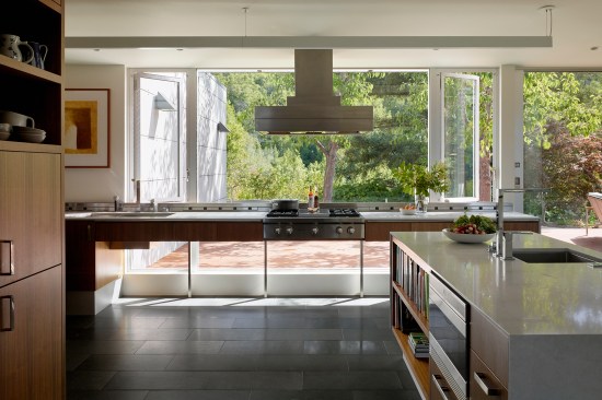 The kitchen was reworked to include a new island (at right) and new cabinetry. The idea for the countertop and range, that it open below to accommodate the client’s wheelchair, was retained from the house’s original design, but now has new products and materials.