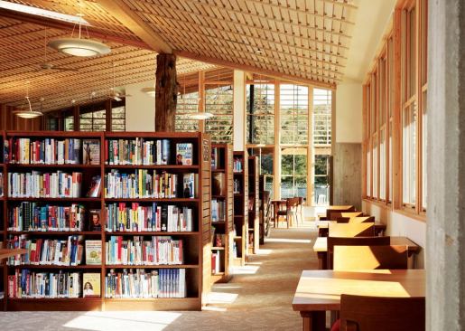 The reading room that holds the main collection of the Portola Valley Library is an airy and light-filled space thanks to floor-to-ceiling windows and skylights. The wall paneling and ceiling slats—elements that appear in all three main buildings—are made from milled Douglas fir roof decking salvaged from the dismantled school.