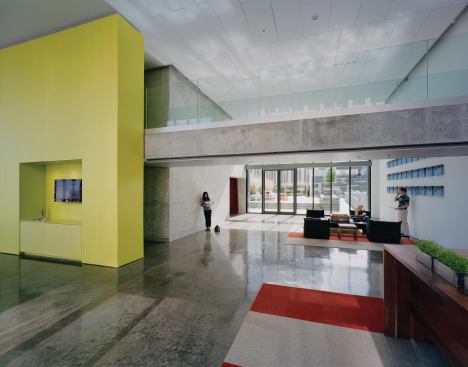 Residents access the ninth floor lobby by elevators from the ground floor (which let out in the red-curtained alcove) and then they must walk through the space to transfer to another bank of elevators to reach the apartments. The circulation path allows for chance interactions with other residents, creating a firmer sense of community in a city unused to high-rise living. Pop colors and exposed concrete surfaces give the interior a modern feel that targets the mainly young tenants, and glass doors lead out to the pool area.