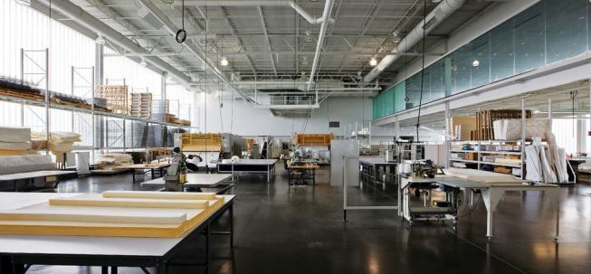 The Serta R&D facility is a double-height space for the study of new and existing products. Raw materials for mattresses, such as springs, padding, and fabric, are stacked on shelves on the south wall, and machinery to construct and run tests on mattresses takes up most of the open floor. The main showroom on the second floor overlooks the work area so that visitors trying out and buying mattresses upstairs can see the product development process.