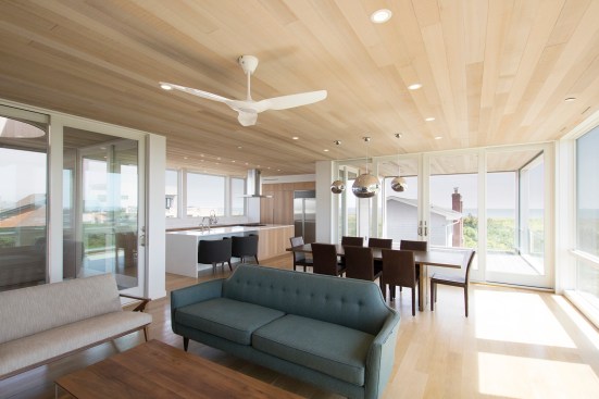 Open living, dining, kitchen wrapped in full height glass and flanked by two covered decks