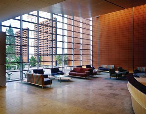 The main lobby has a floor-to-ceiling curtain wall system that admits ample natural light into the reception and waiting areas. A Moeding terra cotta fa?ade continues into the building, where it is lit by wall washer light fixtures hidden above the canted artificial wood acoustical ceiling. Acoustical Wood Ceiling: Armstrong; Woodworks perforated metal ceiling panel in White Maple with a clear finish; armstrong.com - Floor Tile: Oregon Tile & Marble; Jura Stone honed in beige and gray; oregontileandmarble.com