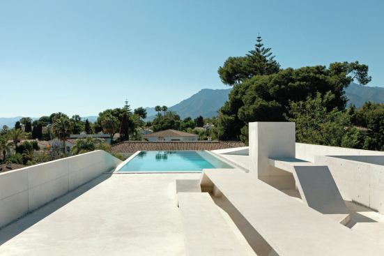 The rooftop pool deck features white concrete benches and views to the Mediterranean Sea beyond.