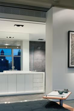 A freestanding white Corian piece subdivides the bath. Its mirror reflects city views from a window in the adjacent master bedroom.