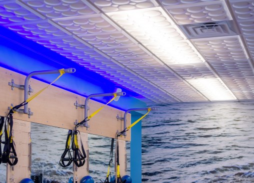 Color LED strips fitted atop the wood wall panels create a deep blue glow around the upper edge of the room, part of the signature look of this Club Pilates chain.