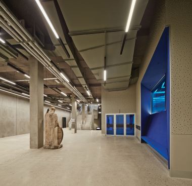 On the basement level, acoustic wallcovering helps control sound in the area outside the main auditorium, seen through the blue glass. Concrete and ductwork are left exposed throughout the structure.