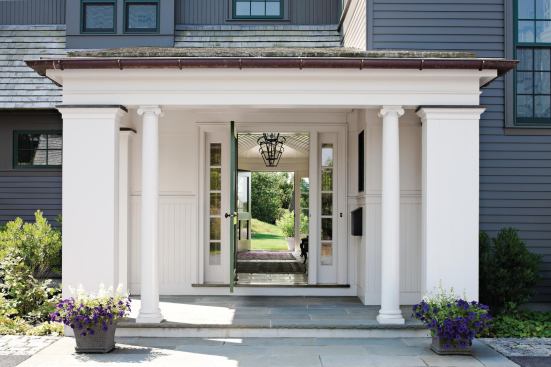 A wide porch shelters and frames the front door, which opens to a vista through the house to the south lawn.