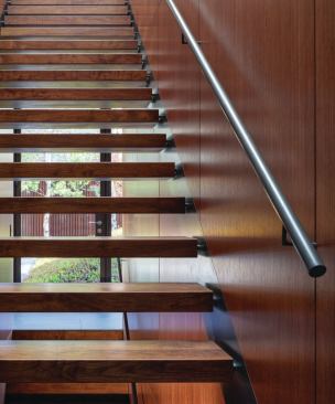 The glazed front door and Cor-Ten gate are visible through the floating treads of the custom staircase that leads to the second level.