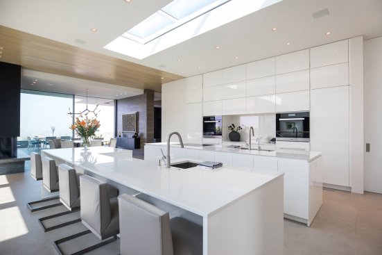 Open plan all white luxury modern kitchen with skylight over the central island breakfast bar.