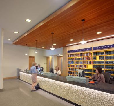The front face of the reference desk is lit with 2W LEDs. Decorative pendants with 75W incandescent lamps create an accent feature above, and 26W BT5 square aperture compact fluorescent downlights provide ambient illumination.