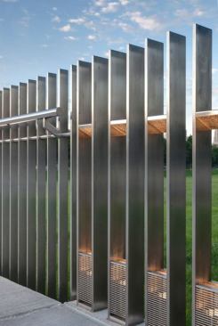 Stainless-steel grilles at the base of the sidewalk lights are hinged for maintenance. Narrow-beam 12W LED cylinders uplight angled, hammered reflectors that create pools of light marching down the path.