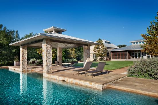 The pool pavilion blends Hill Country limestone masonry with a standing-seam hip roof more suggestive of Gulf Coast environs.