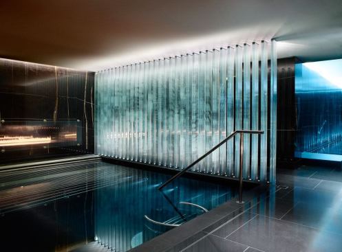 In the pool area, lighting through vertical glass fins creates geometric patterns on the water, the floor and the ceiling.