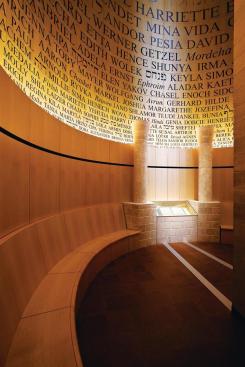 The Room of Remembrance is a double-height volume located on the third floor of the museum. Flanked by Jerusalem stone columns, a book containing the names of those killed during the Holocaust and memories penned by family and community members serves as the focal point of the space. Bent-wood, uplit panels were painted with names of the dead, in English, Yiddish, and Hebrew. First names were used so as to represent as many individuals as possible; the names are 2 1/2 inches high at the base and increase in size as they move toward the ceiling. The names begin in a full, rich black at the base, which turns into a mid-tone black at the top. This was a nod to an idea by a community member to have smoke coming from behind the book of names, a proposal that was not carried out because of fire regulations.
