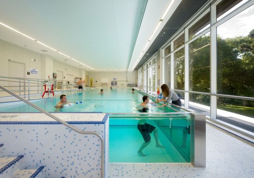 The ground floor includes a therapy pool with transparent glass walls. Floor-to-ceiling windows welcome natural light and provide views to Riverdale Park.