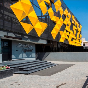 The yellow panels rest on a grey metal mesh forming the base of the façade