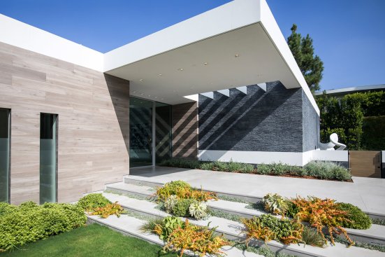 Modern Beverly Hills home front entrance with stacked stone walls, ribbon windows and garden landscape design.