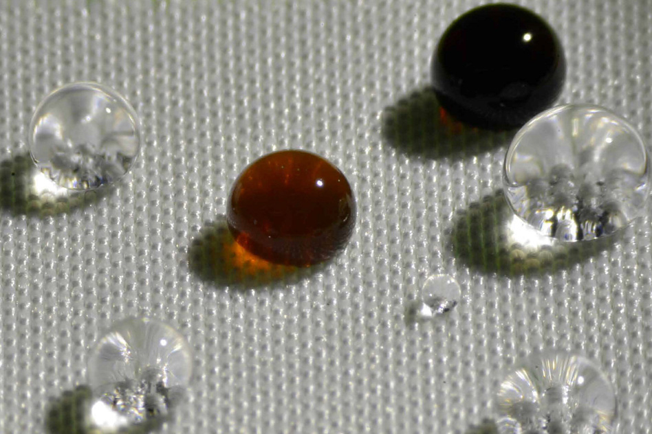 Repellency of different liquids on polyester fabric coated with H1F7Ma-co-DVB: soy sauce (black drop), coffee (brown drop), HCl acid (top left transparent drop), NaOH (bottom right transparent drop), and water (remaining transparent drops).