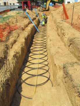 Workers installed a "slinky" earth heat exchanger in one of three identical trenches on the south side of the facility for the geothermal system.