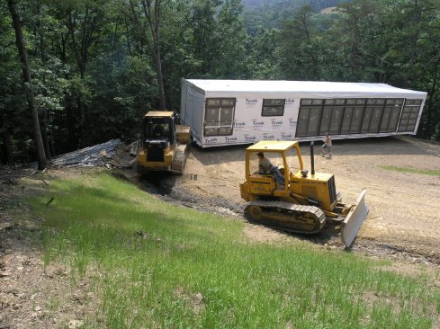 Prefab module being towed up the steep dirt road by dozers.
