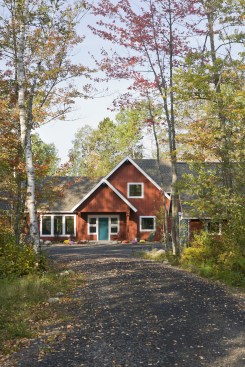 Gravel driveway leading up to very pretty red cabin in the woods
