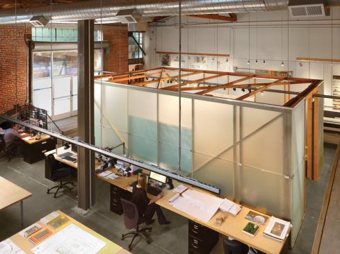 The open-plan studio features 25-foot ceilings, exposed framing, and concrete floors.