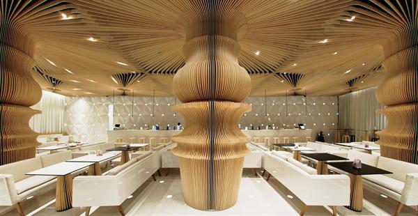 The space is anchored by a series of columns clad in plywood slats that are CNC-routed to emulate a lathe-turned table leg.