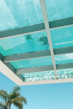 The underside of the cantilevered pool structure is glazed, allowing sunlight to filter through the water to the entry ramp and adjacent terrace below.